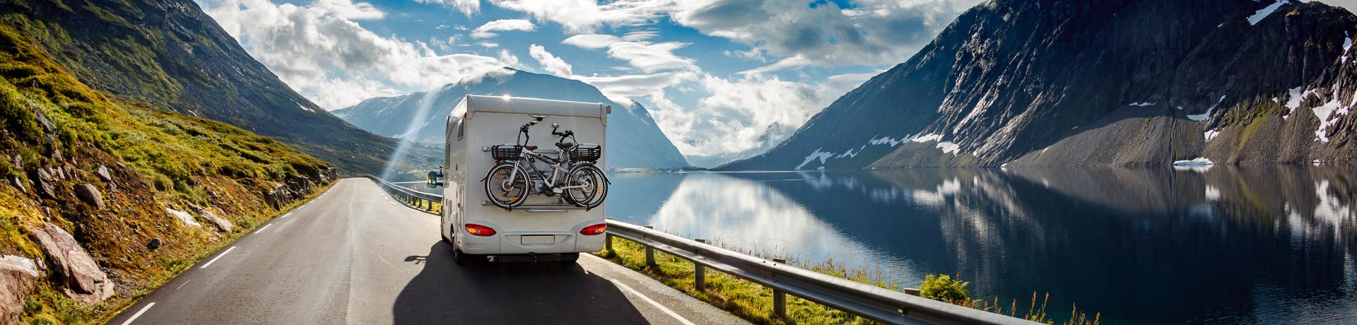 Wohnmobil mit Fahrrädern fährt entlang eines Bergsees.