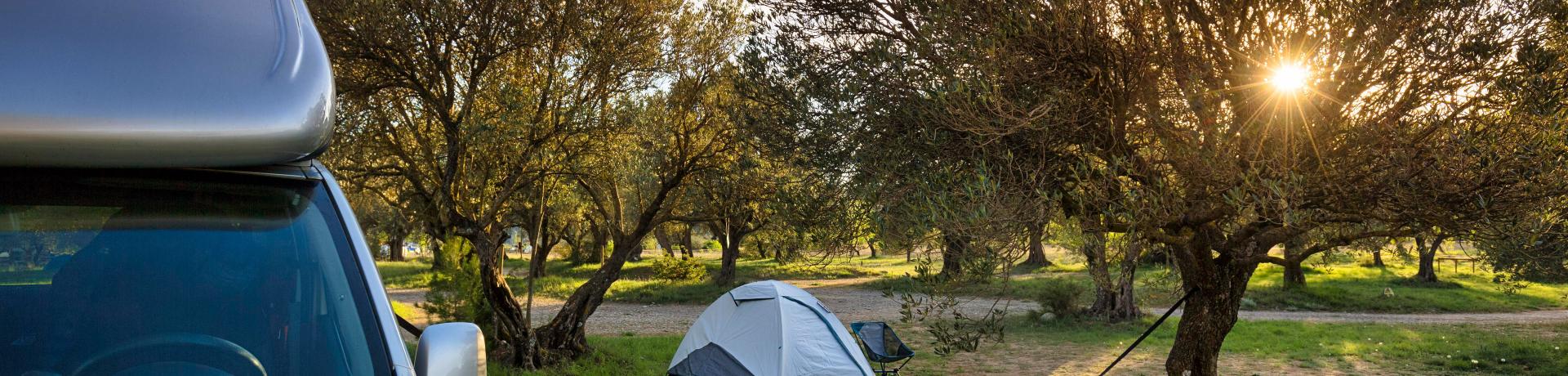 Wohnmobil in einem Olivenhain mit Hängematte und Zelt im Hintergrund.
