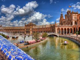 Ansicht des Plaza de España in Sevilla mit Kanal, Booten und Besuchern.