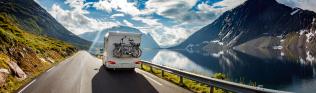 Wohnmobil mit Fahrrädern fährt entlang eines Bergsees.