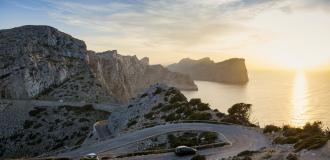 Kurvige Bergstraße in der Serra de Tramuntana auf Mallorca mit Meer und Sonnenuntergang im Hintergrund.