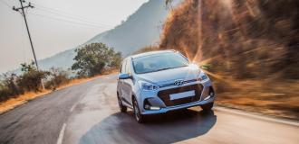 Ein silberner Kombi fährt auf einer kurvigen Straße durch eine Landschaft aus Hügeln und Bäumen.