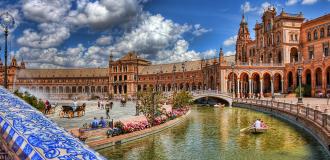 Ansicht des Plaza de España in Sevilla mit Kanal, Booten und Besuchern.