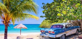 Blauer Oldtimer an einem Strand mit Palmen in Kuba.