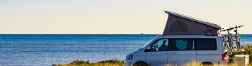 Campervan mit aufgestelltem Dachzelt an der Küste und mit Meer im Hintergrund.