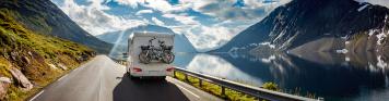 Wohnmobil mit Fahrrädern fährt entlang eines Bergsees.