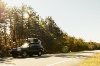 SUV mit Kayak auf Dach fährt auf Waldstraße.