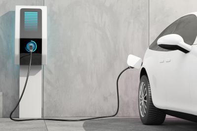 Mit einem Elektroauto sind Sie CO2-neutral unterwegs. Elektroauto wird an einer Ladesäule vor einer grauen Wand geladen.