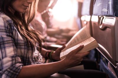 Turbulenzen sind die Ausnahme: Im Flugzeug kann man entspannt lesen, Filme schauen oder schlafen. Eine Frau liest im Flugzeug entspannt ein Buch