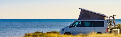 Campervan mit aufgestelltem Dachzelt an der Küste und mit Meer im Hintergrund.