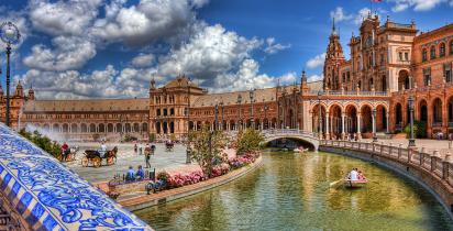 Ansicht des Plaza de España in Sevilla mit Kanal, Booten und Besuchern.