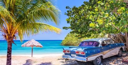 Blauer Oldtimer an einem Strand mit Palmen in Kuba.