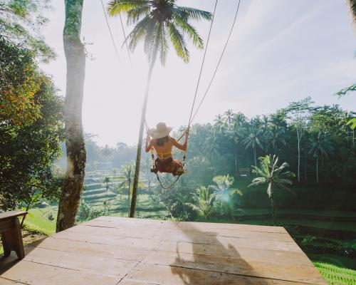 Frau schaukelt über tropischer Landschaft bei Sonnenschein.
