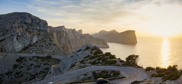 Kurvige Bergstraße in der Serra de Tramuntana auf Mallorca mit Meer und Sonnenuntergang im Hintergrund.