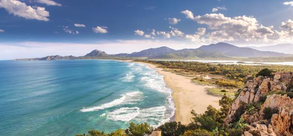 Blick über den Strand von Muravera auf Sardinien mit Bergen im Hintergrund.