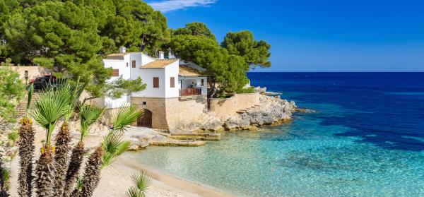 Sonniger Strand der Cala Gat in Cala Ratjada auf Mallorca mit Wohnhaus im Hintergrund.