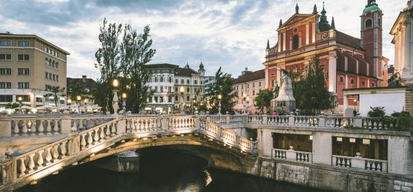 Brücke Tromostovje in Ljubljana am Abend mit Kirche im Hintergrund.