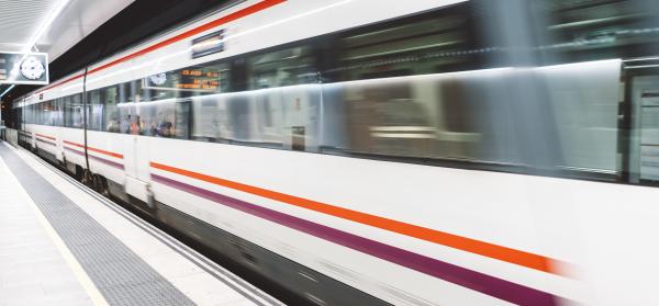 Schnell vorbeifahrender Zug in einem Bahnhof mit leeren Bahnsteigen.