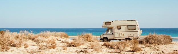 Ein altes Wohnmobil steht auf einem Stellplatz am Meer inmitten mediterraner Vegetation.