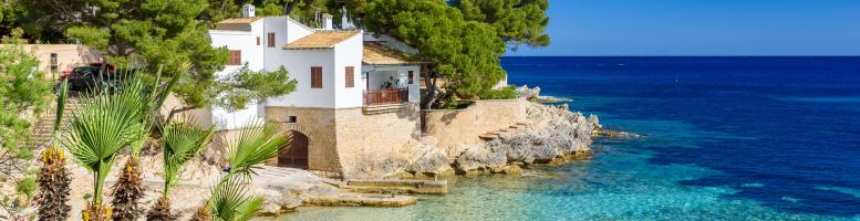 Sonniger Strand der Cala Gat in Cala Ratjada auf Mallorca mit Wohnhaus im Hintergrund.