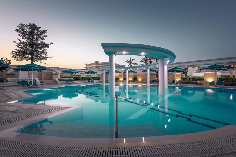Abendstimmung am beleuchteten Pool des Mitsis Grand Hotels auf Rhodos mit eleganten Säulen und Sonnenliegen