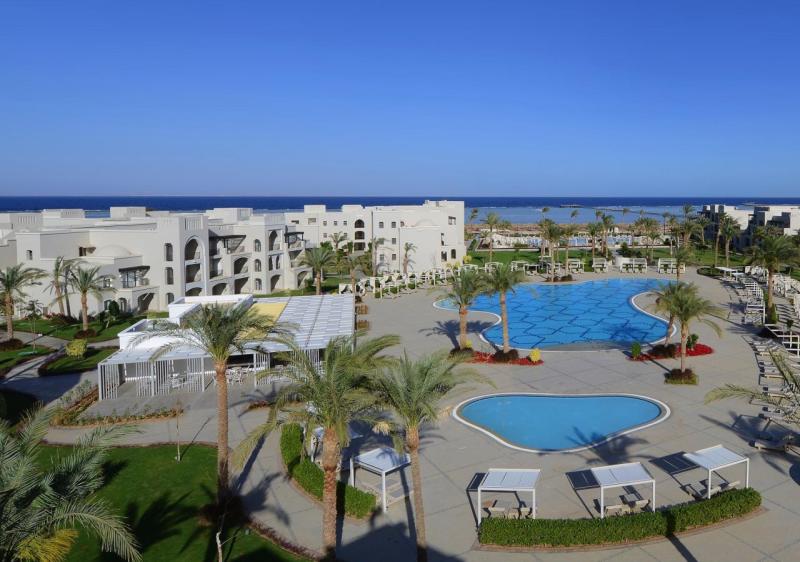 Luxuriöse Hotelanlage mit Pools, Palmen und Blick auf das Meer unter klarem Himmel.