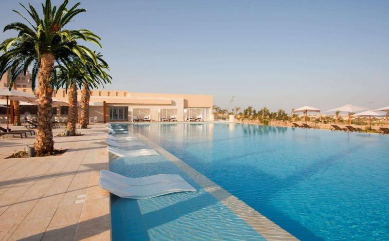 Moderner Infinity-Pool mit Palmen, Liegestühlen und Sonnenschirmen bei klarem Himmel.