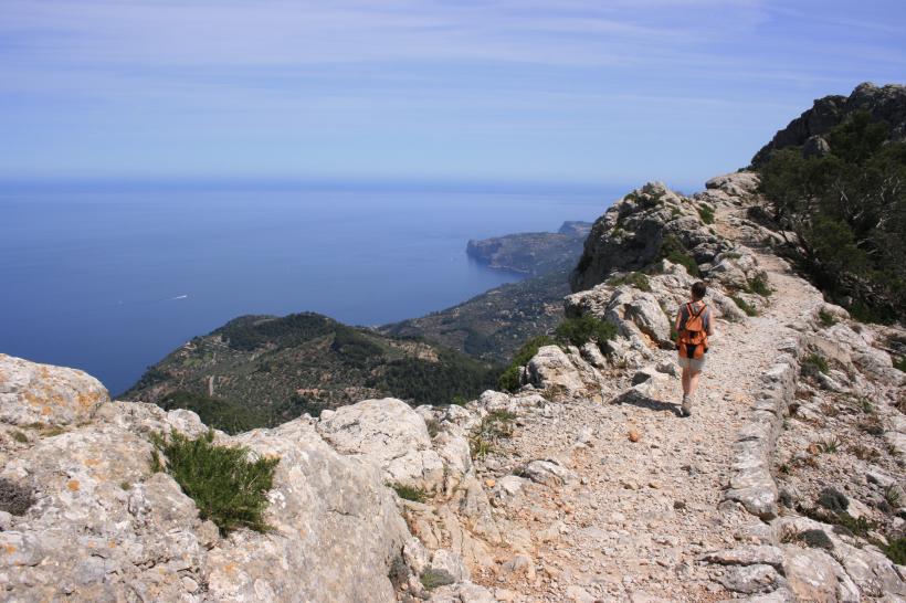 Wanderer auf einem Bergpfad in der Serra de Tramuntana auf Mallorca mit Meer im Hintergrund.