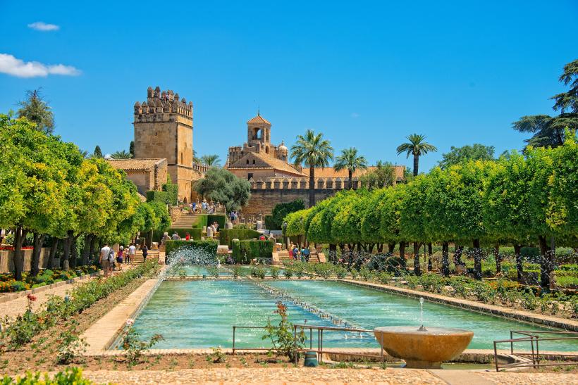 Alcázar von Cordoba mit Brunnen im Vordergrund vor blauem Himmel.