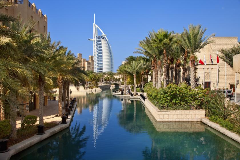Blick auf das Burj Al Arab in Dubai mit Palmen, Wasserkanal und traditioneller Architektur.