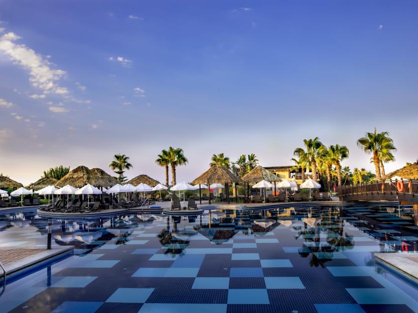 Weitläufige Poollandschaft mit Palmen und Sonnenschirmen im Tui Blue Belek bei Sonnenuntergang in der Türkei