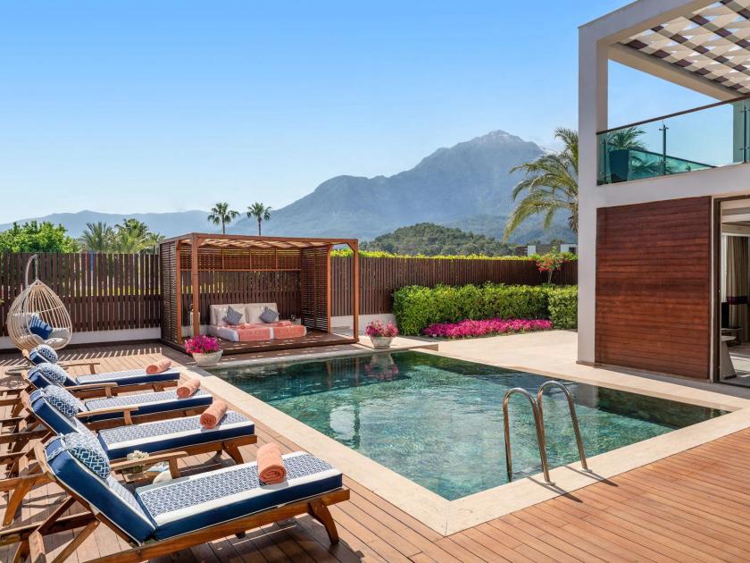 Private Terrasse mit Pool, Sonnenliegen und Pergola, umgeben von Blumen und Bergblick.
