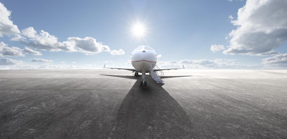 Flugzeug auf dem Rollfeld unter blauem Himmel mit Sonne und Wolken im Hintergrund.